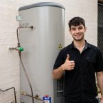 Professional plumber giving a thumbs up next to a hot water service for our Hot Water Price Guide Sydney.
